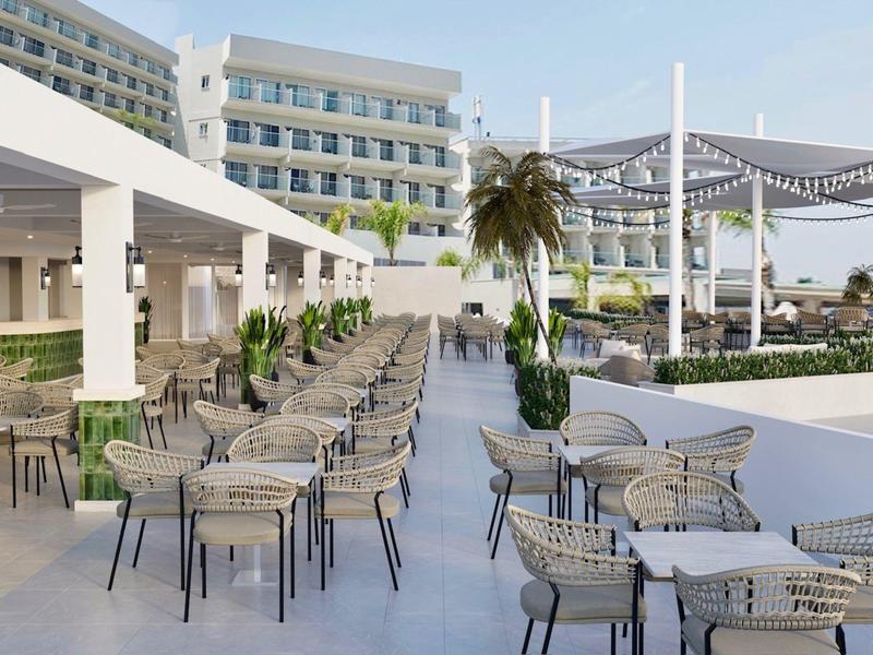 Moderne buitenruimte van een hotel met tafels, stoelen en palmbomen onder zonnescherm.