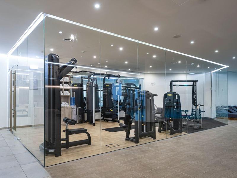 Moderne sportschool omgeven door glazen wanden met verschillende fitnessapparaten en heldere verlichting.