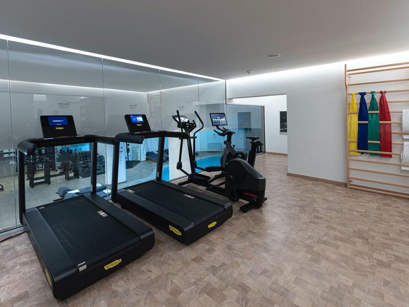Moderne fitnessruimte met loopbanden, hometrainers en kleurrijke matten aan de muur.