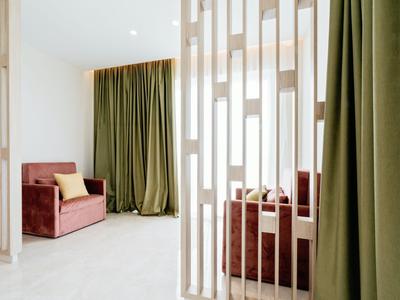 Zona giorno moderna con tende verdi e poltrone rosse dietro un divisorio bianco.