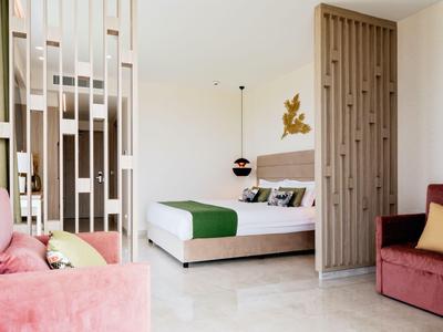 Camera d'hotel moderna con letto matrimoniale, divano rosa e divisorio.