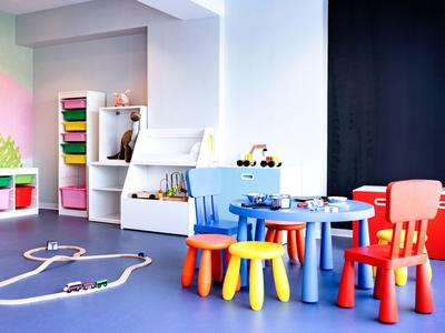 Area giochi colorata con piccoli tavoli, sedie e giocattoli in una stanza luminosa.