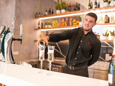 Un barista con camicia nera versa champagne in bicchieri in un bar moderno.