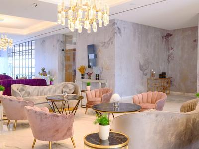 Area lounge elegante con poltrone in velluto, tavoli e illuminazione moderna in tonalità neutre.