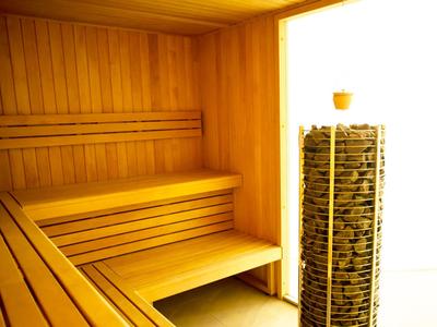 Locale sauna luminoso con panchine in legno e un riscaldatore a pietre vicino all'ingresso.