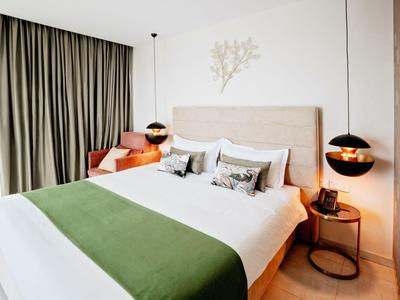 Stanza d'hotel moderna con letto grande, coperta verde e lampade sospese su entrambi i lati.