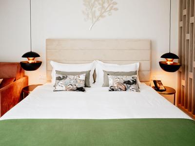 Camera d'albergo moderna con letto grande, coperta verde e lampade sospese