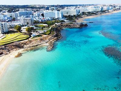 Costa con acqua turchese limpida, spiaggia e edifici bianchi in una zona turistica.