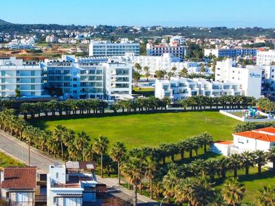Grande complesso alberghiero con edifici bianchi e prati verdi in una città costiera.
