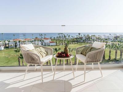 Terrazza con due sedie e tavolo con cesta di frutta, vista su giardino di palme e mare