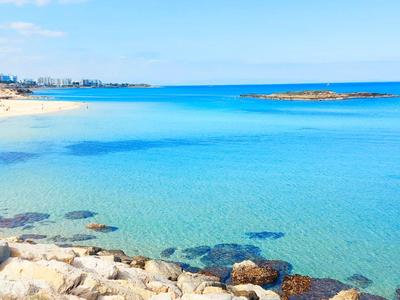 Spiaggia con acqua turchese limpida e rocce in primo piano in una giornata soleggiata