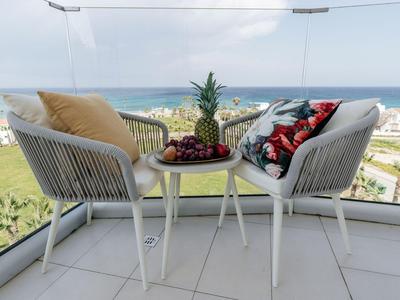 Balcone con due sedie, tavolo con ananas e uva, vista sul mare e sulla spiaggia.