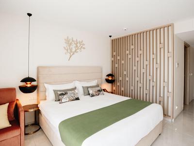 Camera d'hotel moderna con letto matrimoniale, copriletto verde e parete decorativa sullo sfondo.