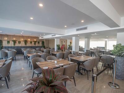 Moderner Speisesaal mit Tischen und Stühlen in hellem, offenem Raum mit großen Fenstern.