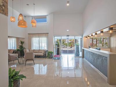 Heller, moderner Empfangsbereich mit Hochglanzboden, Sitzgruppen, Pflanzen und großen Fenstern.