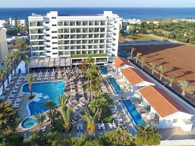 Großes Hotel mit mehreren Pools und Liegestühlen, umgeben von Palmen und Blick aufs Meer.