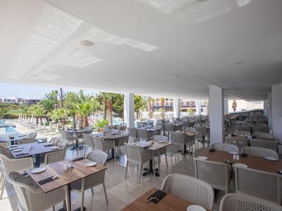 Offener Speisesaal mit Tischen und Stühlen, Blick auf Pool und Palmen im Außenbereich.