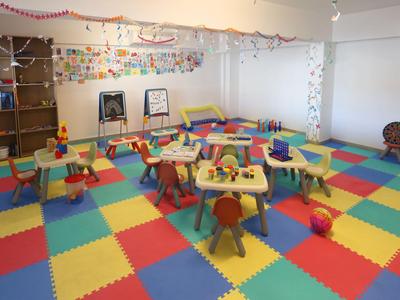 Bunter Kinderspielraum mit kleinen Tischen und Stühlen auf gepolstertem Boden.