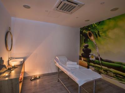 Behandlungsraum mit Massageliege, sanfter Beleuchtung und entspannendem Wandbild mit Buddha und Steinen.