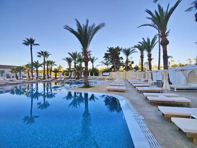 Moderner Hotelpool mit Sonnenliegen und Palmen unter klarem Himmel.