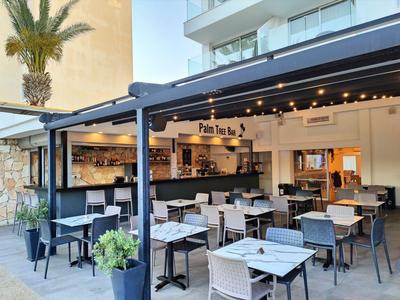 Moderner Außenbereich eines Hotels mit Sitzgelegenheiten unter einer Pergola und Pflanzen.