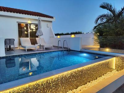 Moderner Hotelpool am Abend mit beleuchteten Steinen und weißen Liegestühlen.