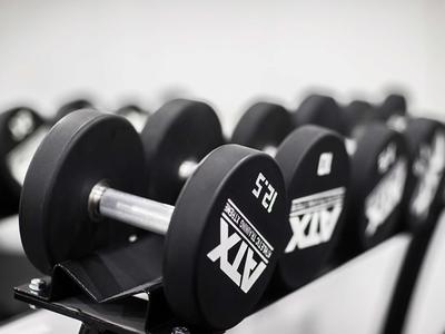 Schwarze Hanteln mit Gewichtsetiketten in einem Fitnessstudio auf einem Regal.