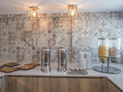 Küche mit hellbraunen Schränken, weißer Arbeitsplatte und gemusterten grauen Fliesen an der Wand.