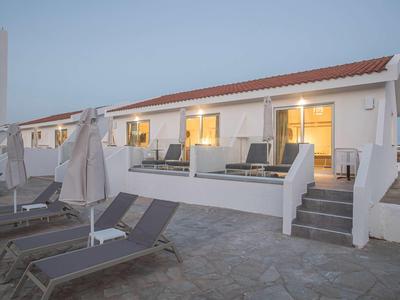 Einreihige Häuser mit weißen Wänden und roten Dächern, davor Liegestühle und geschlossene Sonnenschirme.