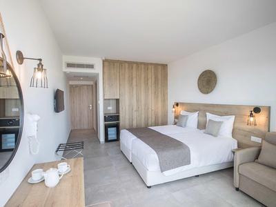 Helles Hotelzimmer mit Doppelbett, Sofa, großem Spiegel und Schrank mit Mini-Kühlschrank.