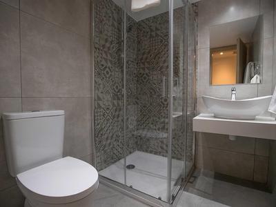 Kleines Badezimmer mit weißer Toilette, Glas-Duschkabine und rechteckigem Waschbecken mit Spiegel.