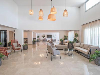 Helles Hotellobby mit modernen Sesseln, Sofas, Pflanzen und hängenden Lampen.