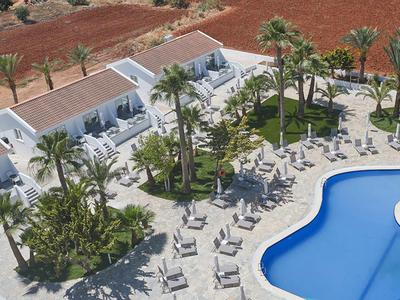 Hotelanlage mit blauem Pool, Palmen und weißen Liegestühlen auf der Terrasse.