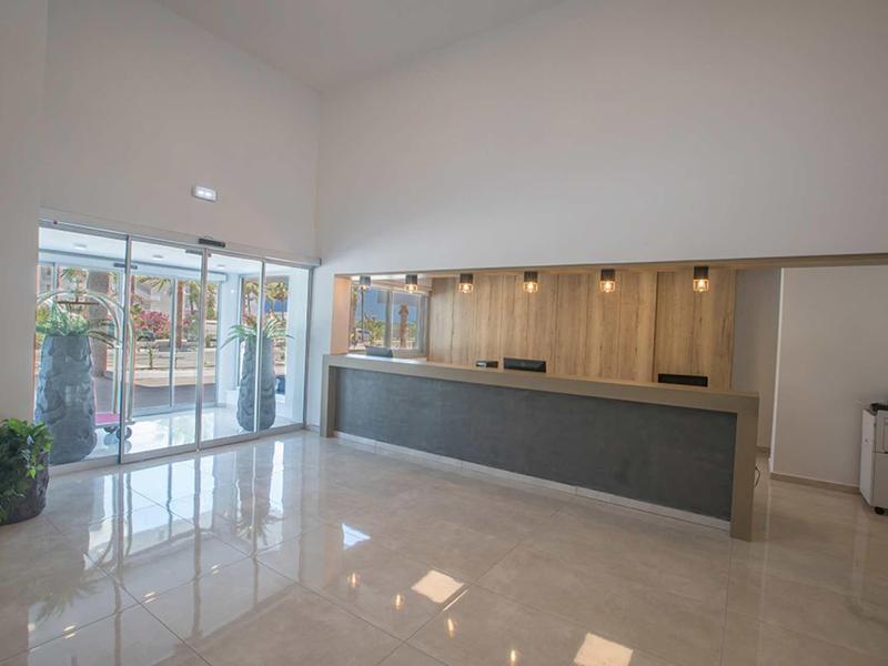 Moderner Empfangsbereich mit grauer Theke, hellen Wänden, großem Fenster und glänzendem Marmorboden.