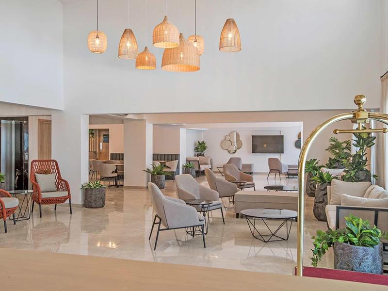 Helles, modernes Hotel-Lobby mit Sesseln, Tischen, Pflanzen und warmen Hängeleuchten.