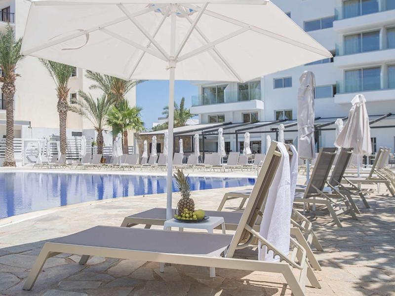 Poolbereich mit Liegestühlen, Sonnenschirm, Palmendekor und modernen Wohngebäuden im Hintergrund.