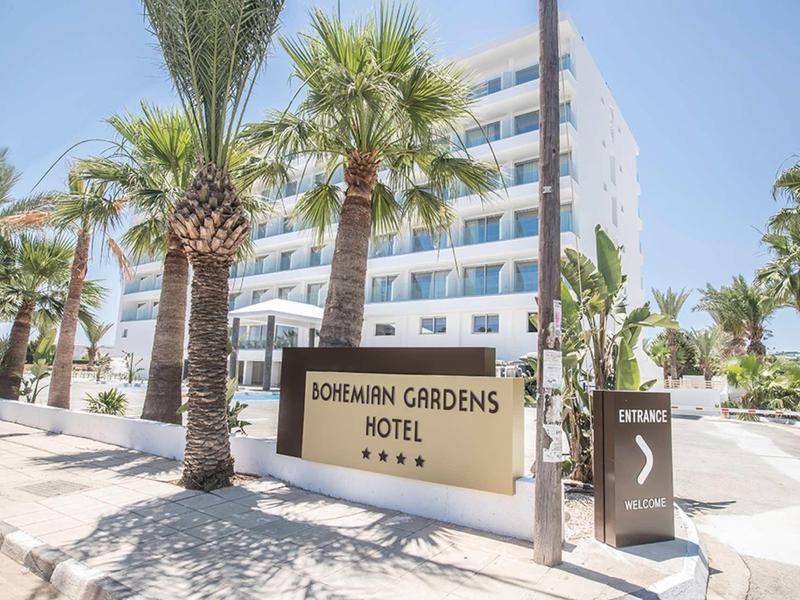 Modernes mehrstöckiges Hotelgebäude mit Palmen und Schildern im hellen Sonnenlicht.