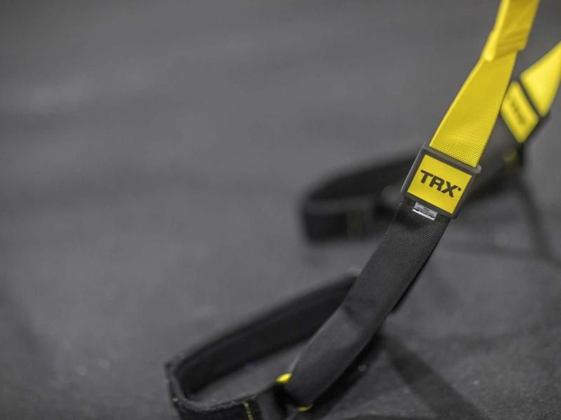 Nahaufnahme von gelben TRX-Trainingsbändern mit schwarzen Haltegriffen auf grau strukturiertem Boden.