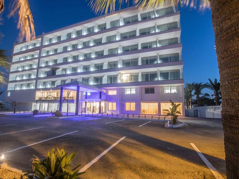 Mehrstöckiges Hotelgebäude bei Nacht mit beleuchteten Balkonen und Parkplätzen im Vordergrund.