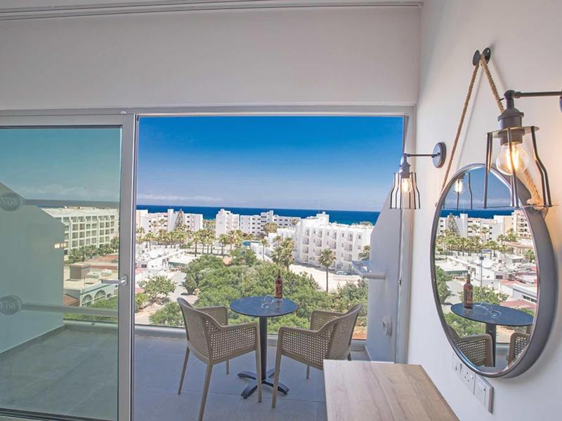 Balkon mit Tisch und zwei Stühlen, Blick auf weiße Gebäude und blauen Himmel.