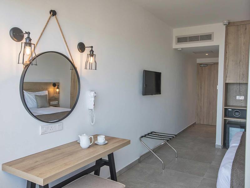 Helles Hotelzimmer mit rundem Wandspiegel, Holztisch, Wandlampen und Fernseher an der Wand.