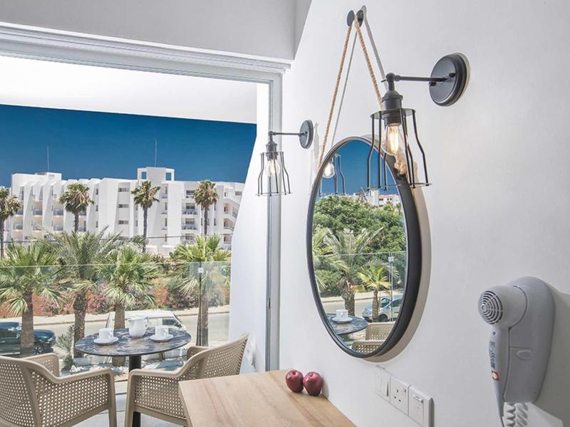 Moderner Essbereich mit Spiegel, Stühlen und Blick auf Palmen und weiße Gebäude unter blauem Himmel.