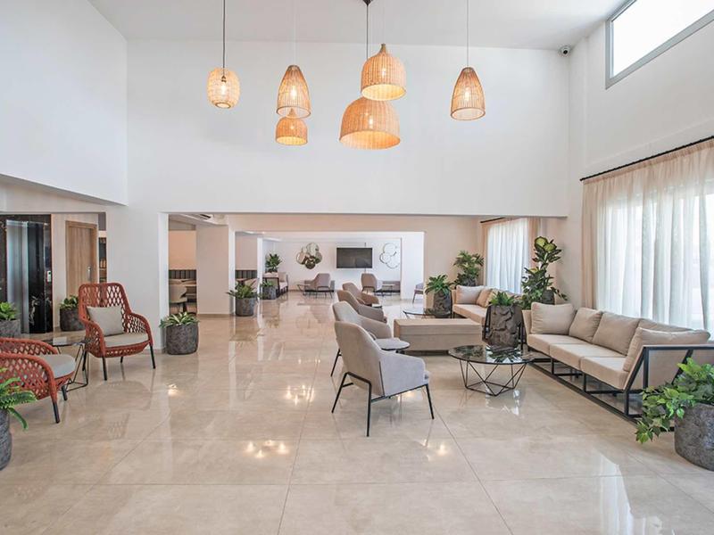 Heller, offener Wohnraum mit cremefarbenem Boden, modernen Sesseln, Sofas und vielen Pflanzen.