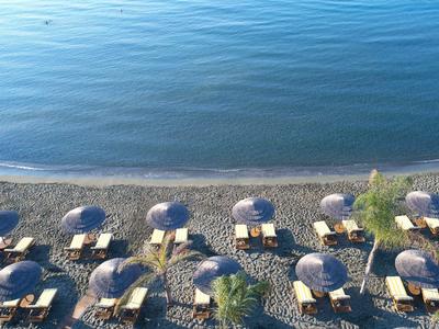 Beach with umbrellas and sun loungers beside calm, blue water.