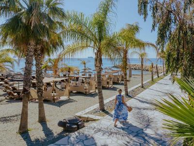 Strandpromenade mit Palmen, Sitzgelegenheiten und einer Person in sommerlicher Kleidung.
