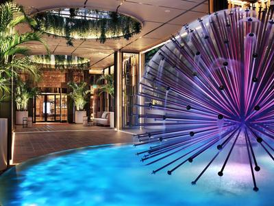 Moderna recepción de hotel con plantas, escultura de agua redonda e iluminación artística.