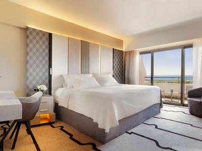 Moderna habitación de hotel con cama grande, escritorio y vistas al mar a través de grandes ventanas.