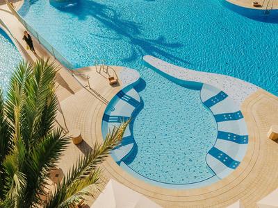 Piscina climatizada con terraza soleada y palmeras en un resort vacacional.
