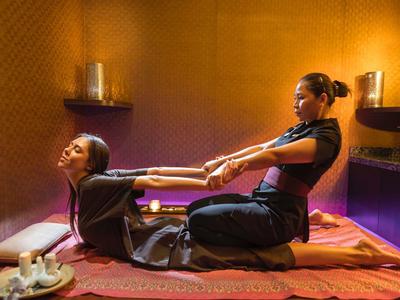 Two women performing traditional Thai massage in a warmly lit room.