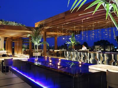 Modern illuminated bar with pool and seating in a hotel lounge at night.